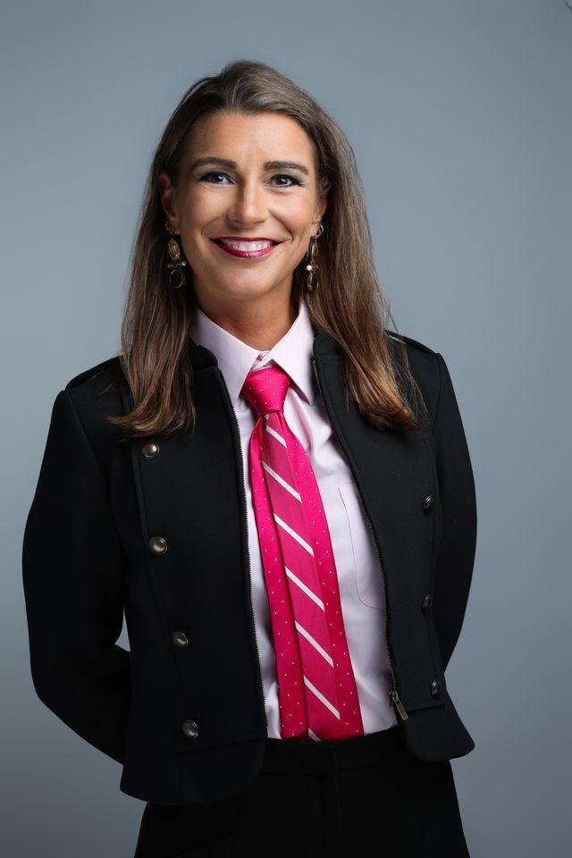 Sarah N. Dimmich in a black jacket and magenta tie, studio portrait